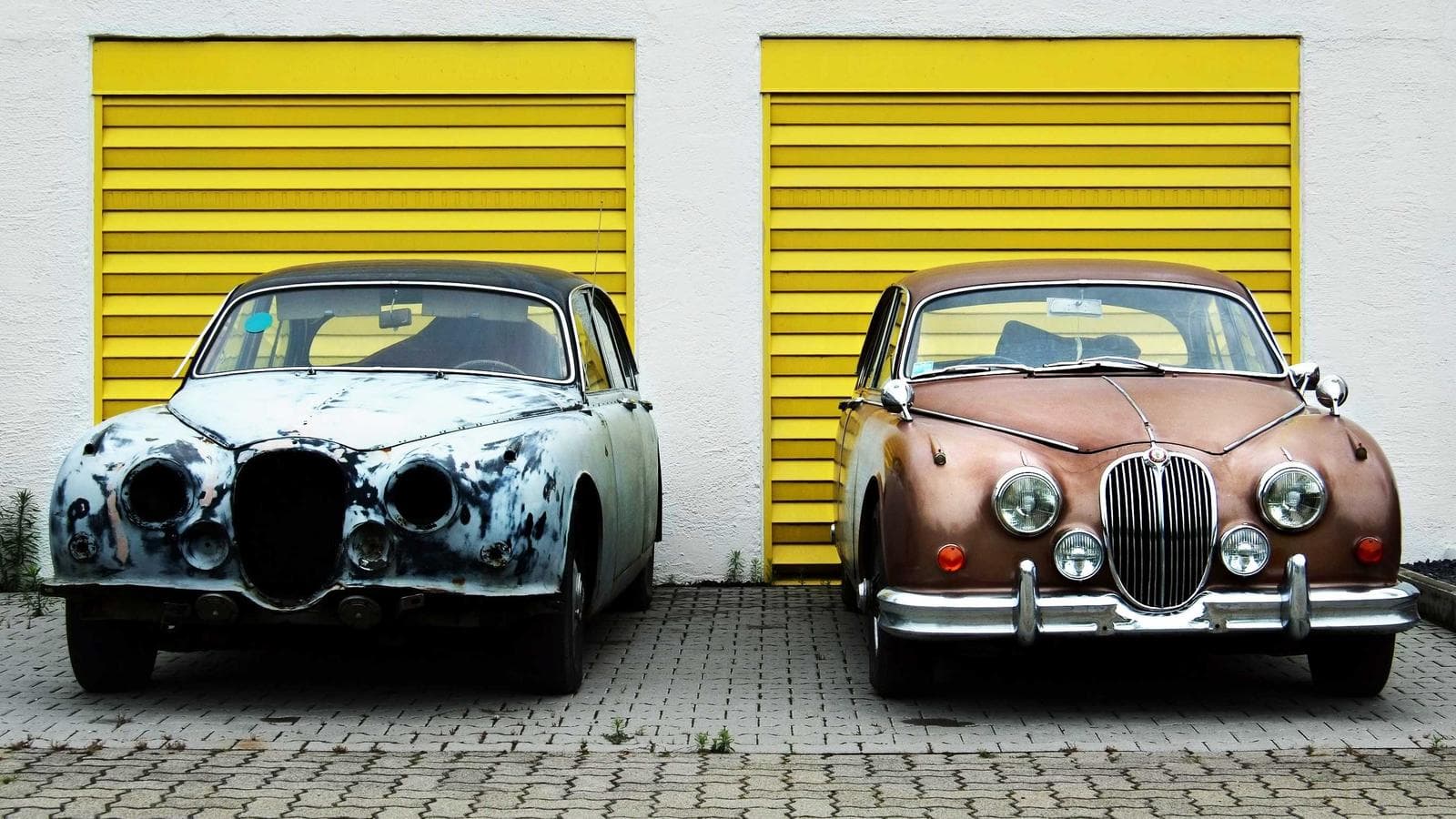 Two restored classic cars parked in front of yellow workshop doors